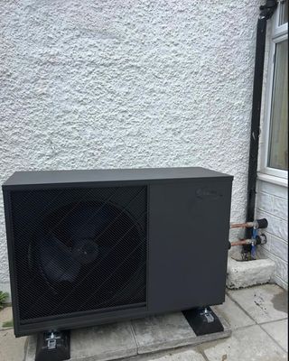 Grant air source heat pump unit installed on paving slabs against a white rendered wall.