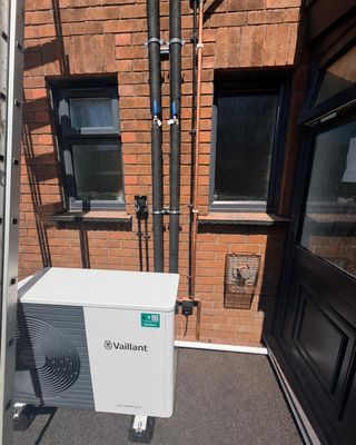 A Vaillant aroTHERM plus unit on the van tail lift outside a brick terraced house.